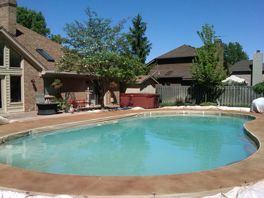 A stained pool deck in a backyard of a house